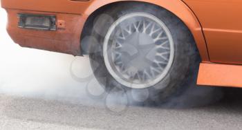 Smoke from under the wheels of the car .