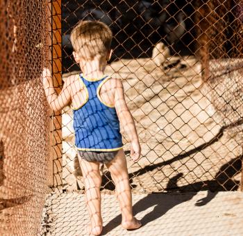 Little boy near a metal grid fence .