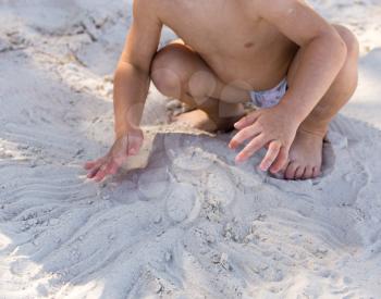 Hands of a boy playing in the sand .