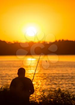 Fisherman with a fishing rod at sunset .