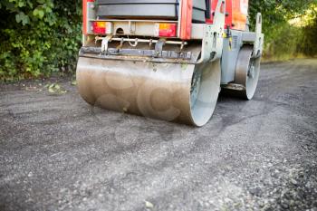 heavy machine rolls a new asphalt road .