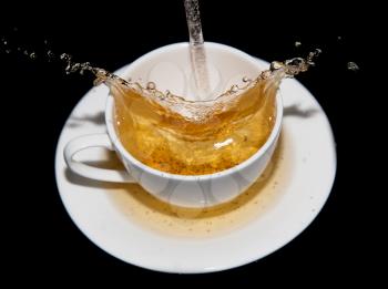 tea being poured into a saucer with splashes on a black background