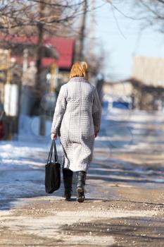 a woman with a bag goes on the road in winter