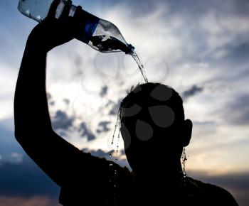 man pours water on his head in the sunset