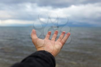 man's hand on a background of the sea with clouds