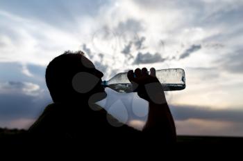 silhouette of a man drinking water at sunset