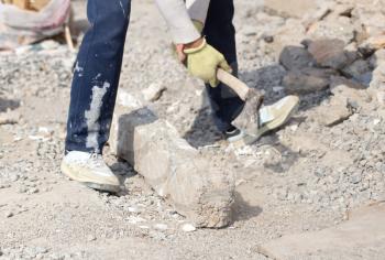 Worker breaks concrete with an ax at the construction site .