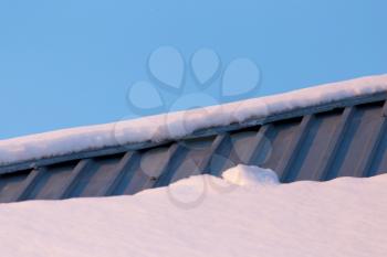 Snow on the roof of the house at sunset .