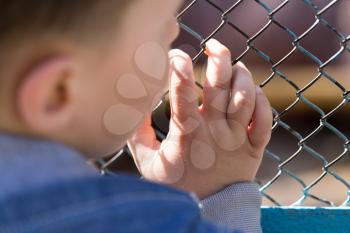 The boy stands near the metal fence .