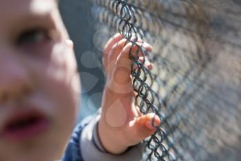 The boy stands near the metal fence .