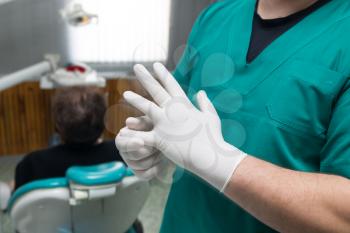 Doctor dentist puts on white gloves in the clinic .