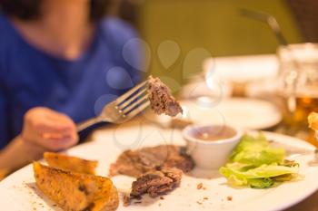 Girl eating meat with salad in a restaurant .