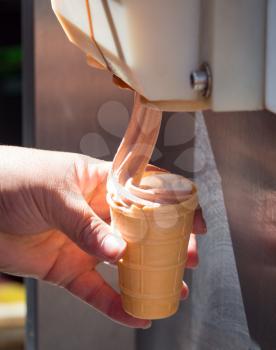 The seller pours ice cream into a wafer cup .
