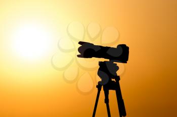 Silhouette of a camera on a tripod at sunset .