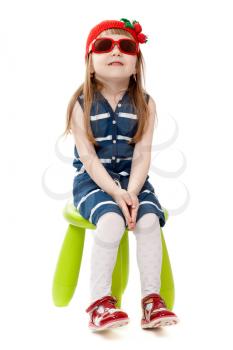 A girl of four years old sitting in a chair wearing sunglasses, isolate on white