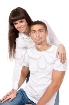 Smiling young couple sitting together, posing in studio on white, looking at camera
