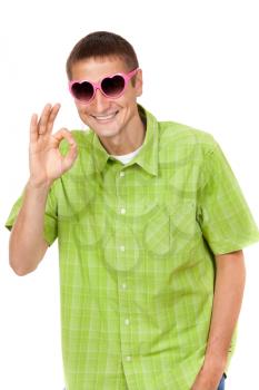Humorous portrait of a young man in a pink sunglasses, heart-shaped sign shows OK. Studio, isolate on white background.