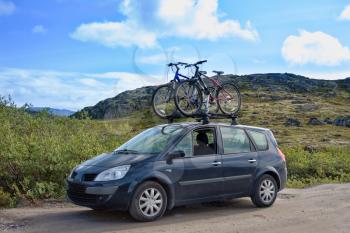 two bicycles mounted on roof of car against mountain and sky