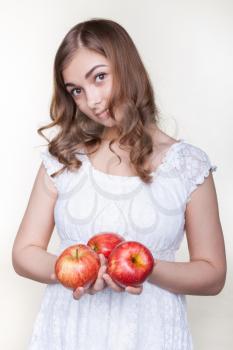Beautiful young girl with three apples in their hands, in the studio on a gray background