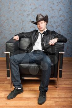 Brutal man in a cowboy hat sitting in leather chair in a luxurious interior