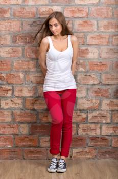 Shy girl casual design in red pants against a brick wall