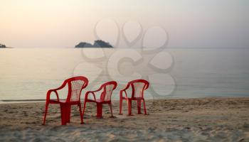 three red chair on an empty beach. sunset