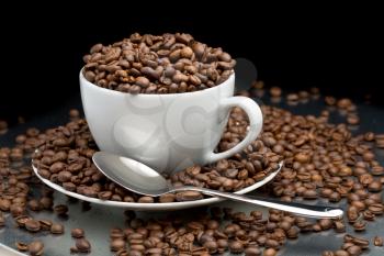 Cup and saucer full of coffee beans with a spoon on a black background