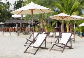 Sun beds and umbrellas on the beach on a background of the jungle