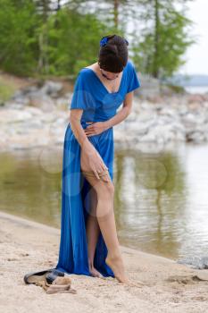 Beautiful girl in a blue dress stockings strips on the lake in the woods.
