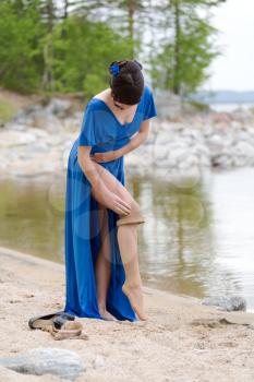 Beautiful younge girl in a blue dress stockings strips on the lake in the woods