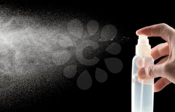 Man hand with a spray bottle of water on a black background.