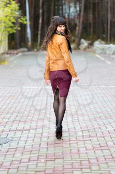Slender girl goes through the autumn alley and turns around, smiles