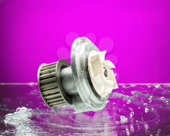 Auto parts, engine cooling pump in spurts of water on purple gradient background.