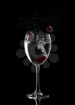 Cocktail splash, with red cherries splashing in to a wine glass, on black background