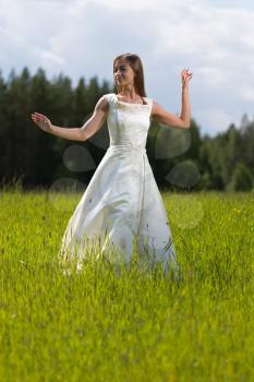 young girl in a wedding dress dancing in the field.