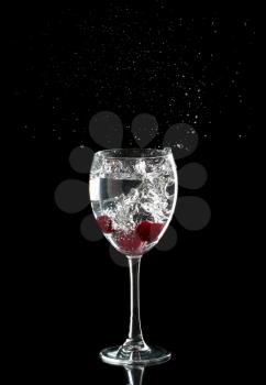 Three cherries in a glass drops splashing on a black background.