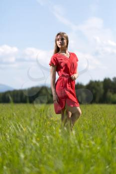 Beautiful girl in a red dress in a field on a sunny day, the sky with clouds.