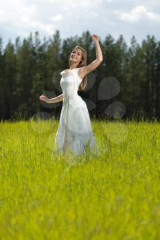 young girl in a wedding dress smiling and dancing in a field.