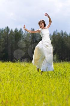woman in a wedding dress jumping in a field with a smile