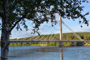 Bridge in Rovaniemi, day, summer, blue sky and clouds. Through the branches of the birch
