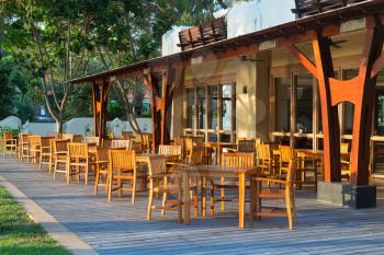 Empty restaurant with wooden furniture in the sunset light of the sun.