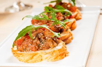 fresh tipycal italian bruschetta with tomato and arugula on top