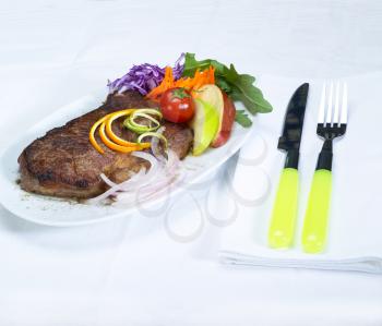 fresh juicy beef ribeye steak grilled with lemon and orange peel on top and vegetables beside