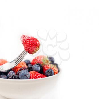 srawberry on a fork with sugar crust and bowl of mixed berries on white background