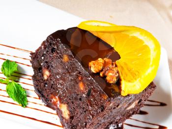 fresh baked delicious chocolate and walnuts cake with slice of orance on top and mint leaf