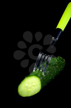 fresh cucumber cutted in half with fork over black background