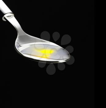 olive oil poured on a spoon over black background