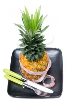 pineapple on a black plate with tape meter,knife and fork isolated on white background