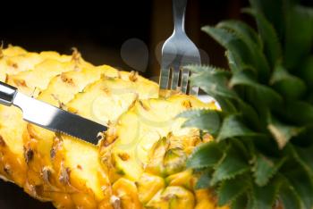 ripe vibrant pineapple sliced on a black plate with knife and fork