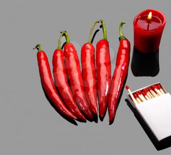 fresh red chili peppers  with matches and lighted red candle over grey reflective surface